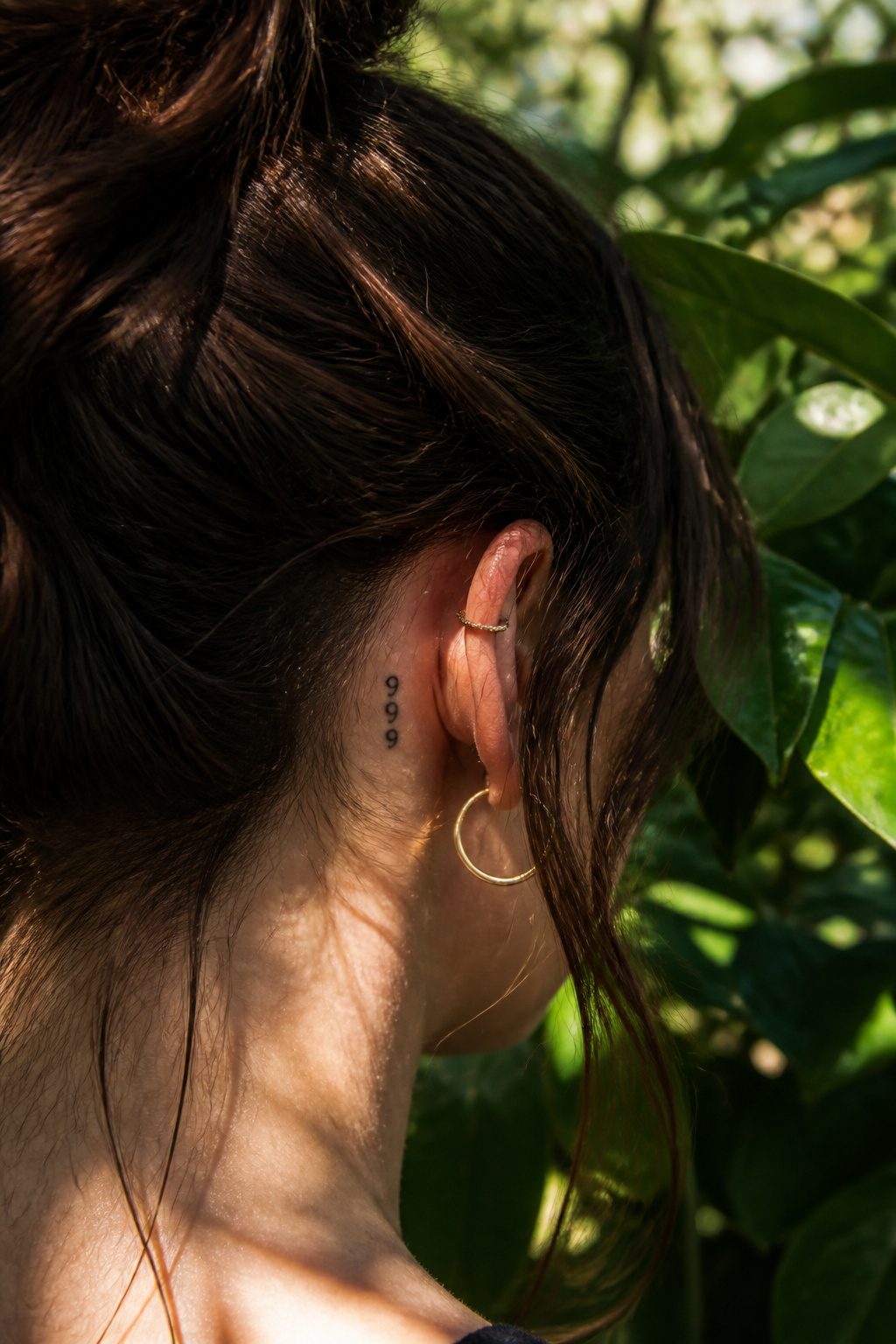 A 999 tattoo placed behind a person's ear in fine line design.