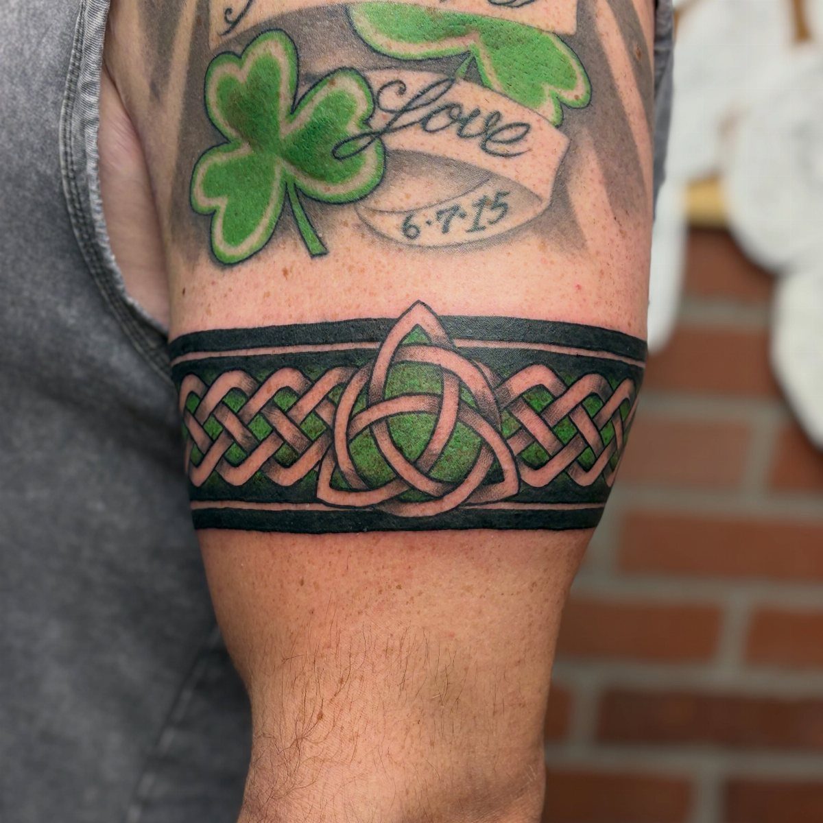 7 Arm Band Colored Tattoo Designs for Men in 2026 1 A man's arm featuring a green and black Celtic knotwork armband tattoo.