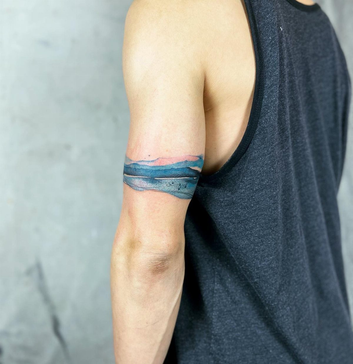 7 Arm Band Colored Tattoo Designs for Men in 2026 5 A man's arm displaying a colorful landscape armband tattoo with blue and pink hues.