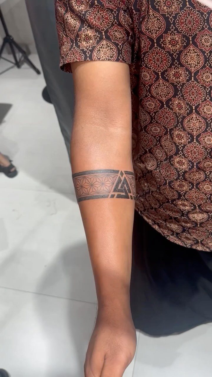 7 Arm Band Colored Tattoo Designs for Men in 2026 4 A person's forearm displaying a black ink geometric armband tattoo with intricate dotwork patterns.