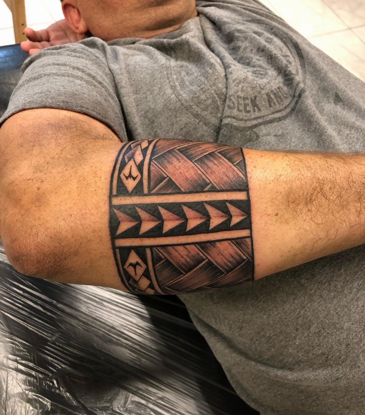 7 Arm Band Colored Tattoo Designs for Men in 2026 3 A man's arm displaying a detailed Polynesian style geometric armband tattoo with dark patterns.