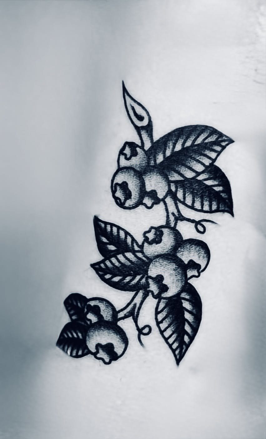 8 Blueberry Tattoo Ideas for Arms, Collarbones and Small Spaces 5 A black ink tattoo of a blueberry branch with leaves and berries on skin.