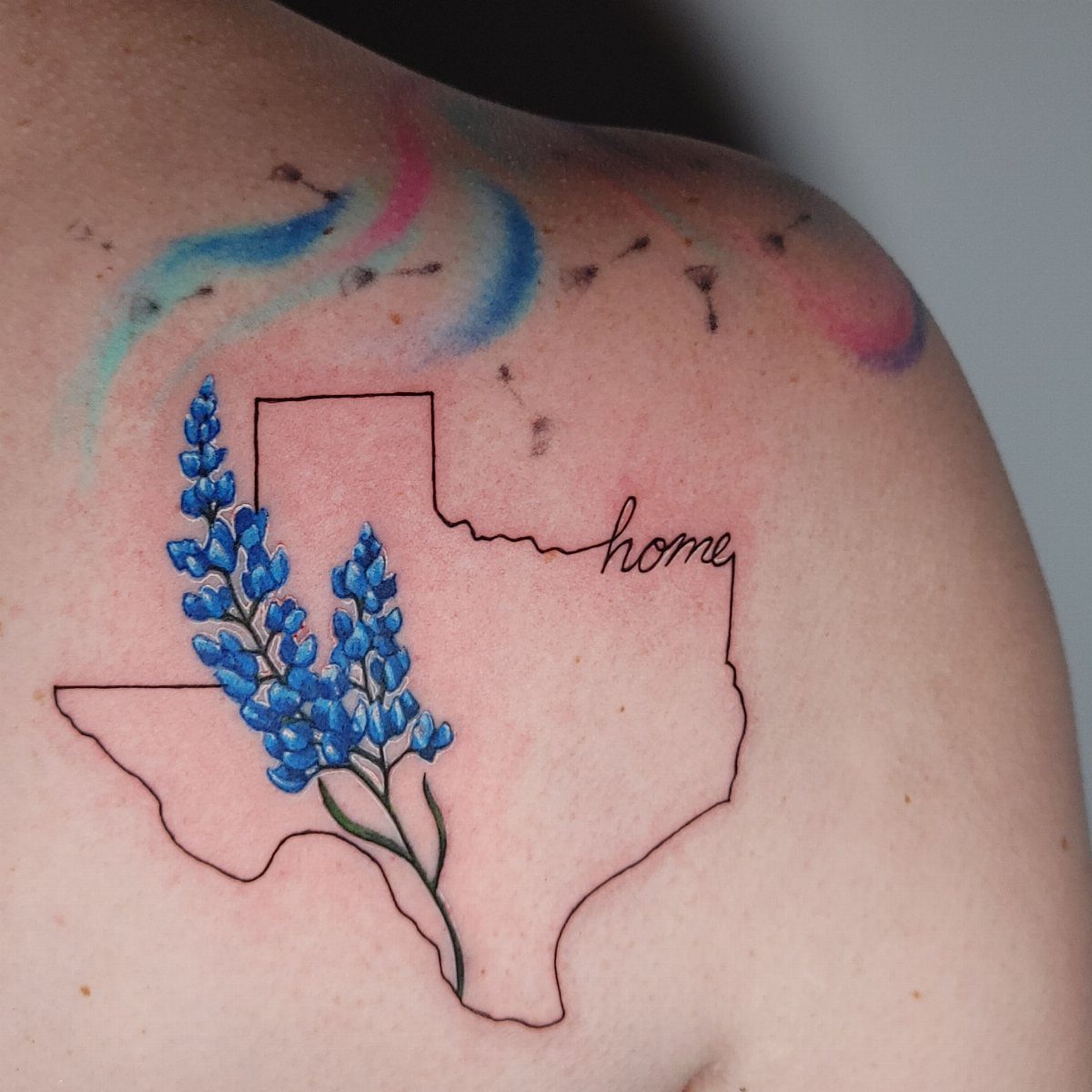 A tattoo of the Texas state outline with bluebonnet flowers and the word home.