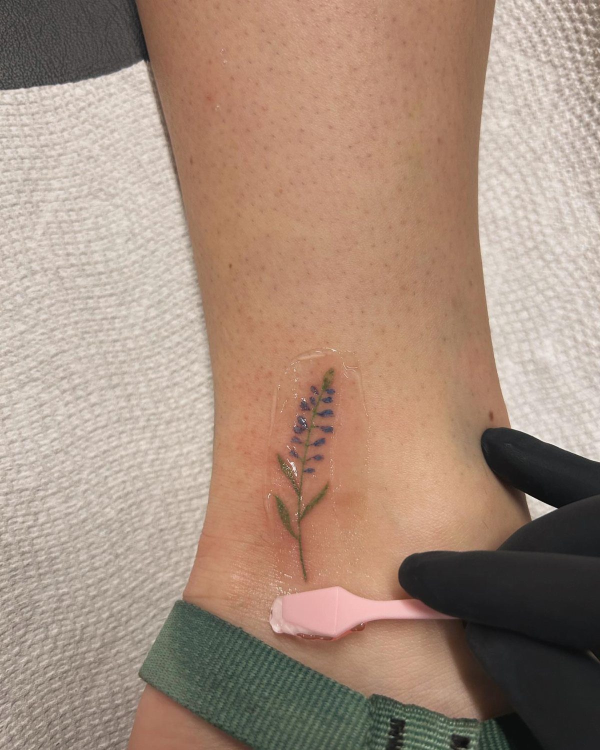 A fine line bluebonnet tattoo on a person's ankle under a clear protective film.