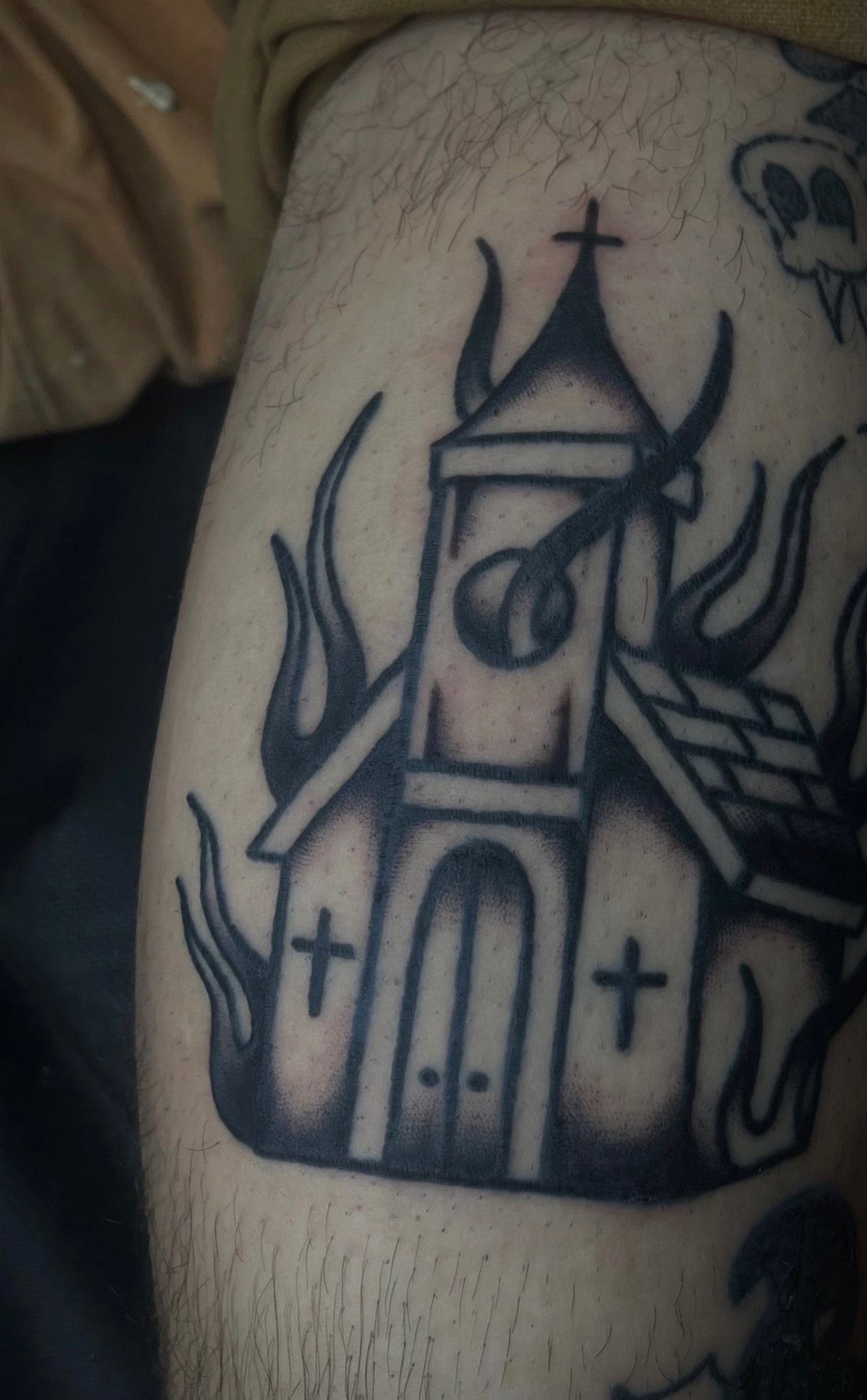 6 Burning Church Tattoo Ideas for Dark, Dramatic Ink 5 A black ink tattoo of a simple church engulfed in stylized flames on a person's leg.