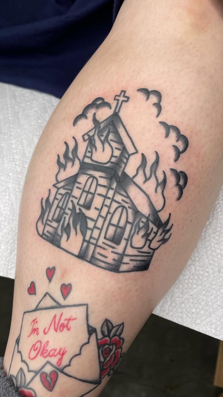 6 Burning Church Tattoo Ideas for Dark, Dramatic Ink 2 A black and grey tattoo of a burning church with a cross on a person's leg.