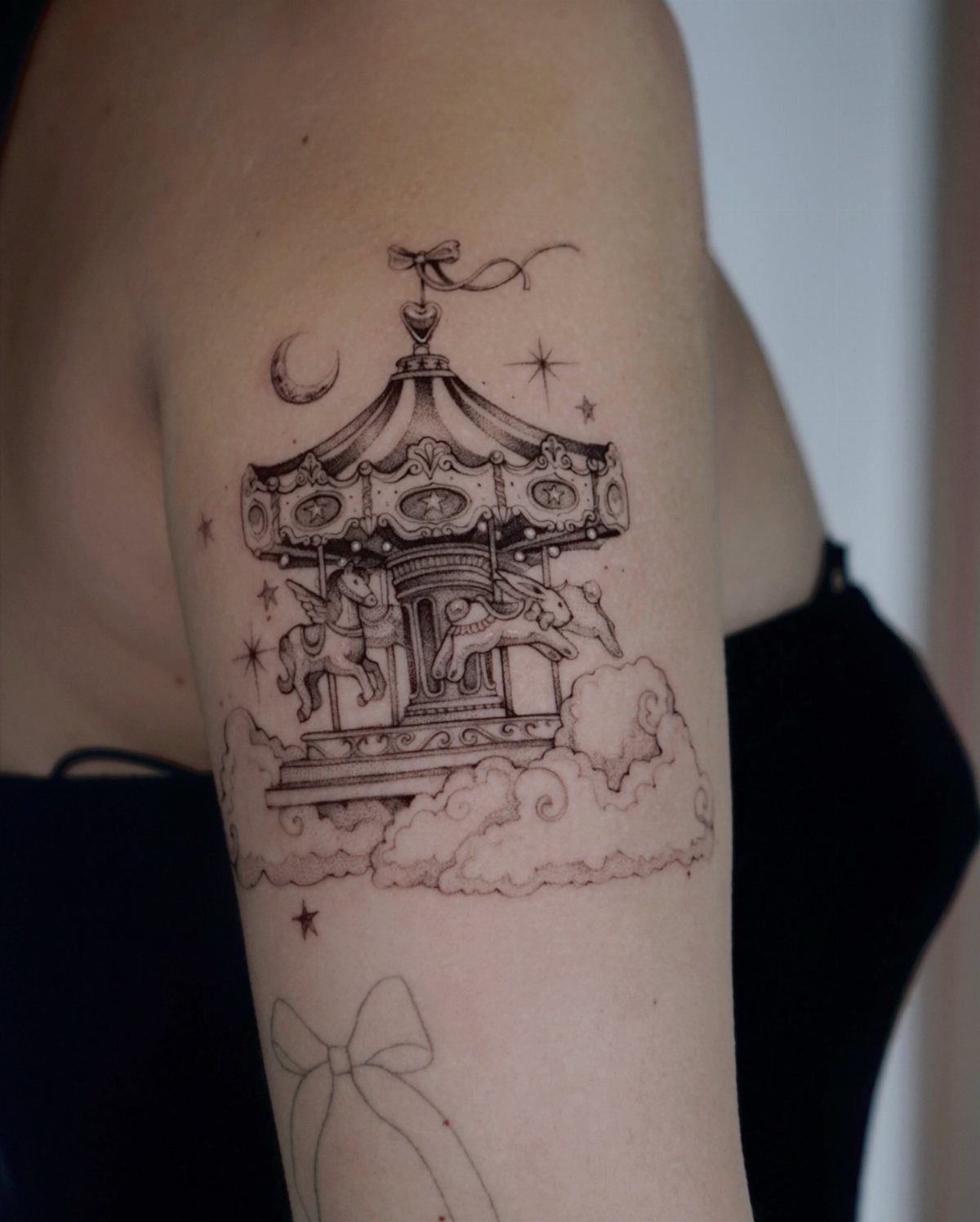 A black ink tattoo of a carousel with horses, stars, and a crescent moon on skin.