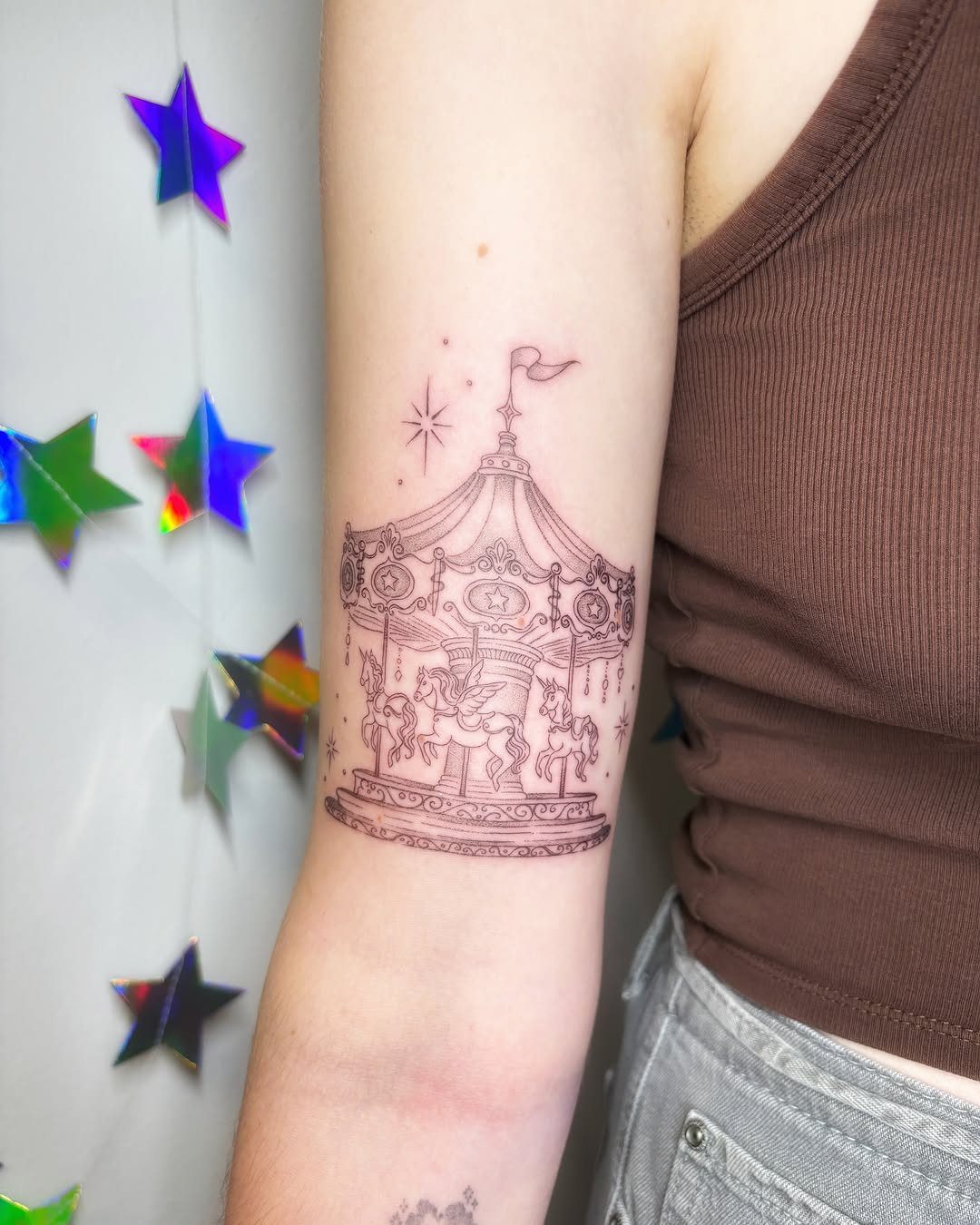 A fine line reddish ink tattoo of an ornate carousel with horses on a person's arm.