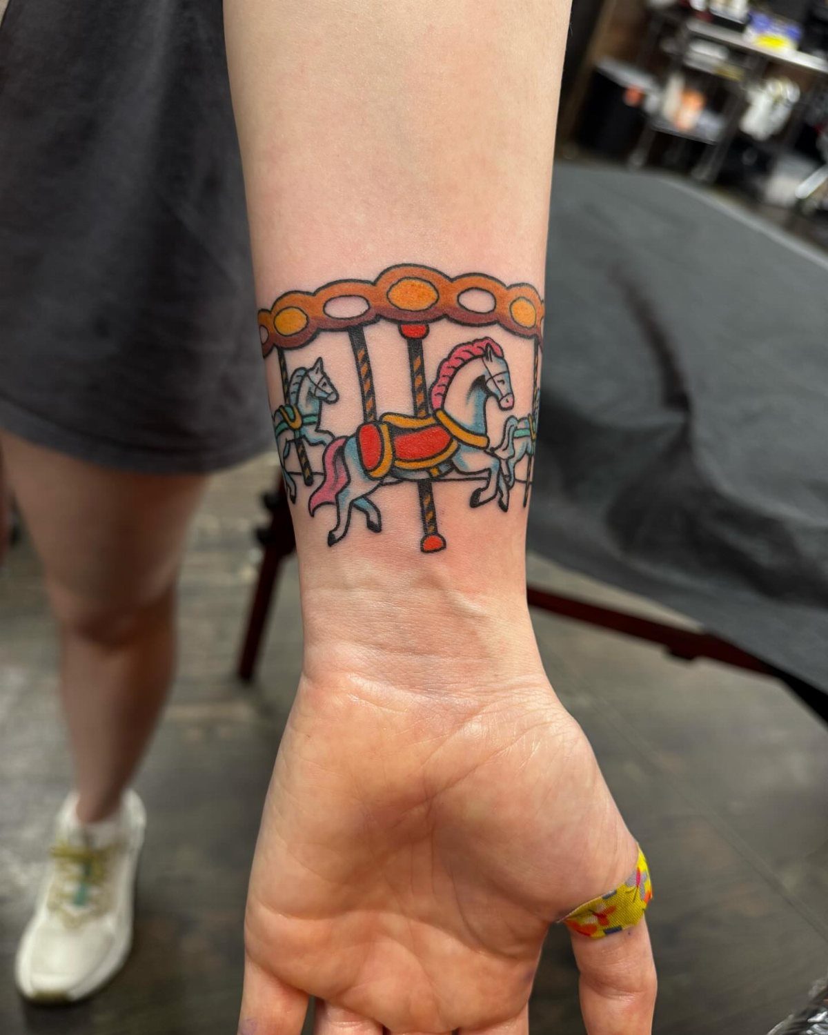 A colorful carousel tattoo with multiple horses wrapped around a person's forearm.