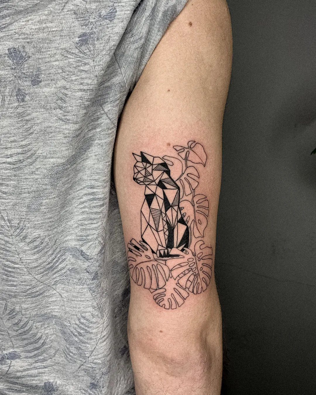 Cat Tattoo with Pattern: 8 Bold Design Ideas to Consider 2 A geometric cat tattoo with botanical leaf patterns on a person's arm.
