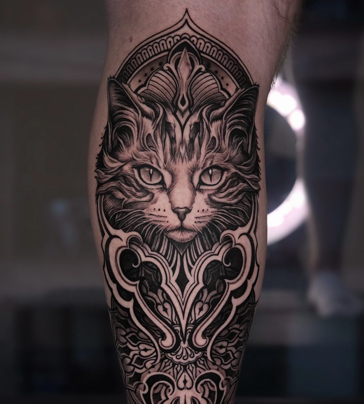 Cat Tattoo with Pattern: 8 Bold Design Ideas to Consider 4 A detailed black and grey cat head tattoo surrounded by intricate mandala patterns on a leg.