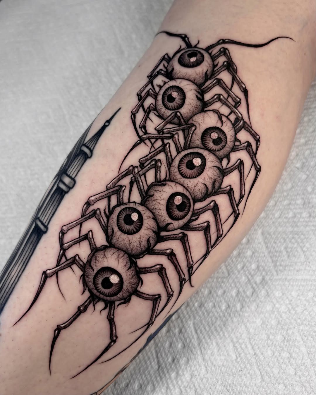 A black ink tattoo of a centipede with human eyes on each segment on an arm.