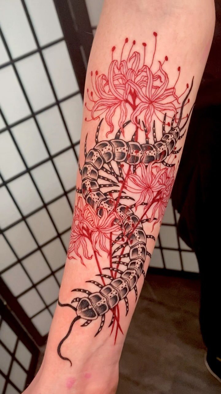 A centipede tattoo intertwined with red spider lily flowers on a person's forearm.