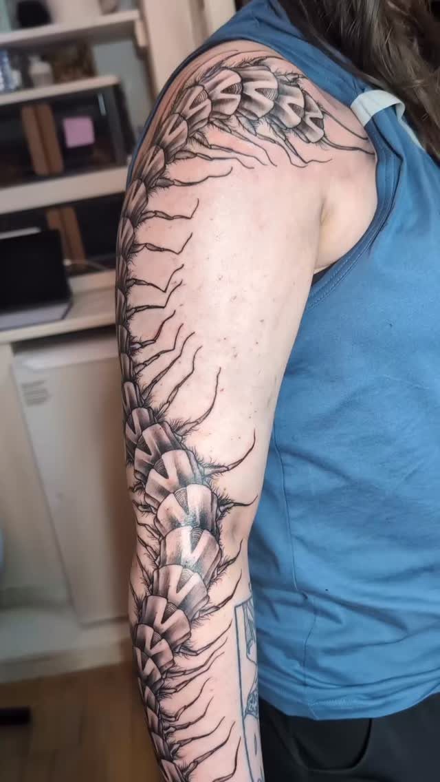 A large black and grey centipede tattoo wrapping around a person's arm and shoulder.