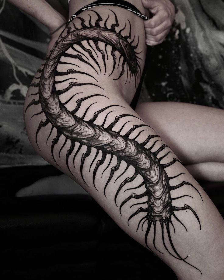 A large black and grey centipede tattoo wrapping around a person's thigh.
