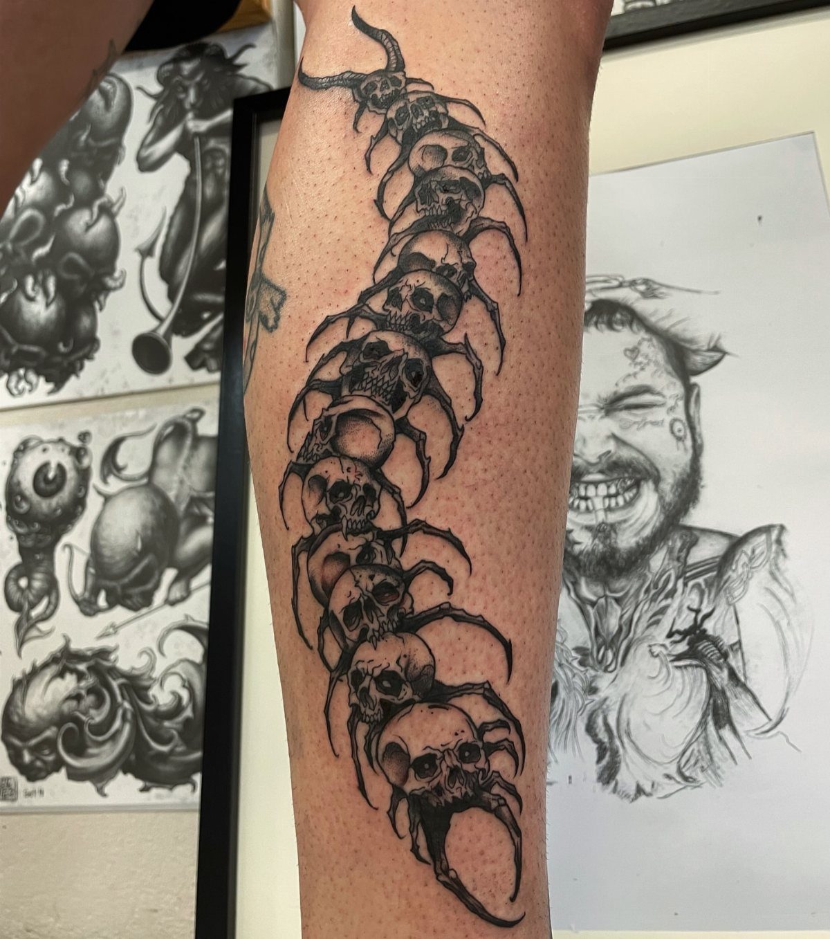 A black ink tattoo of a centipede made of human skulls on a person's arm.