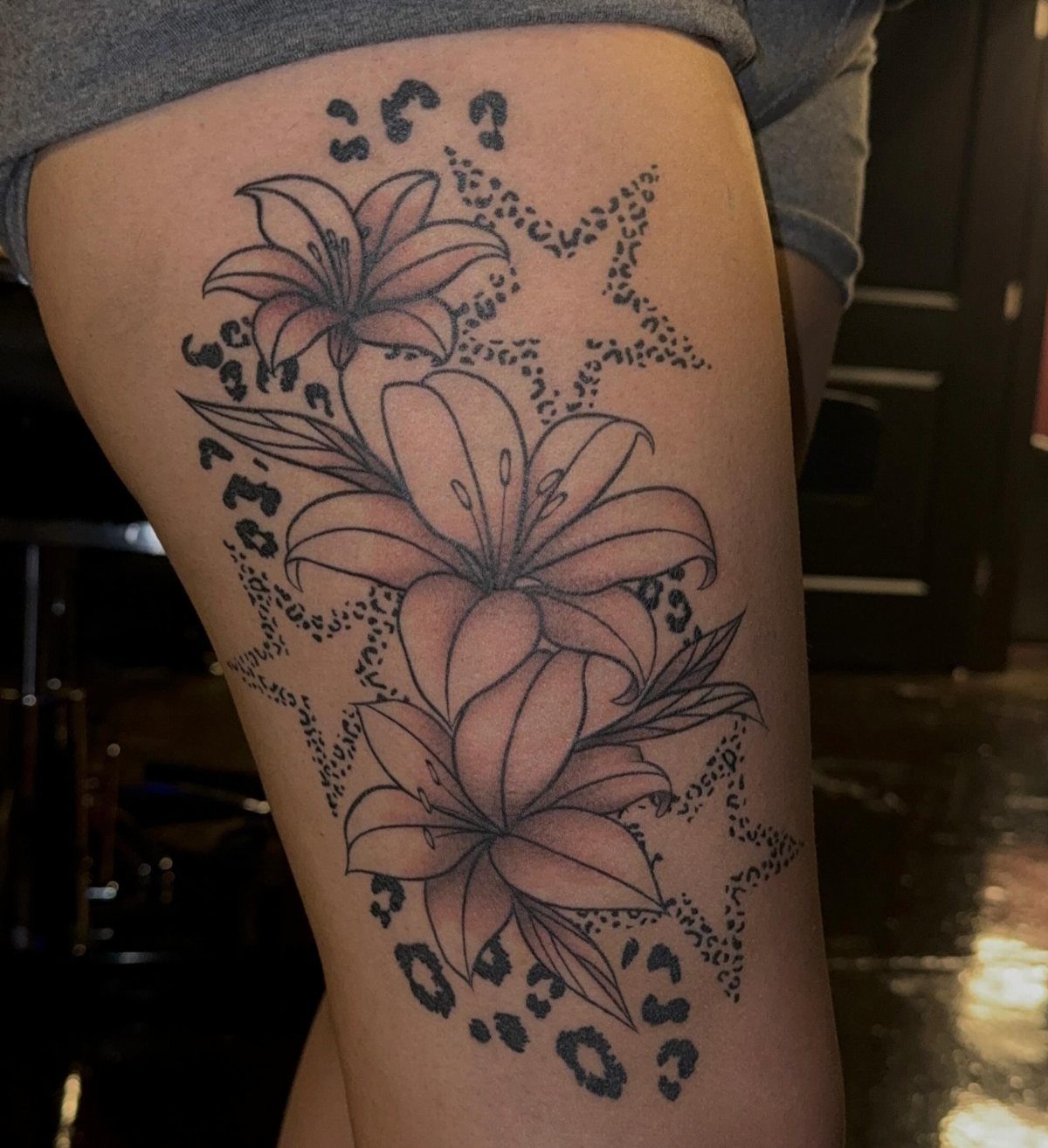 Cheetah Thigh Tattoo: 6 Ideas for Women Who Want Bold Ink 1 A black ink tattoo of lilies and cheetah print spots on a person's thigh.