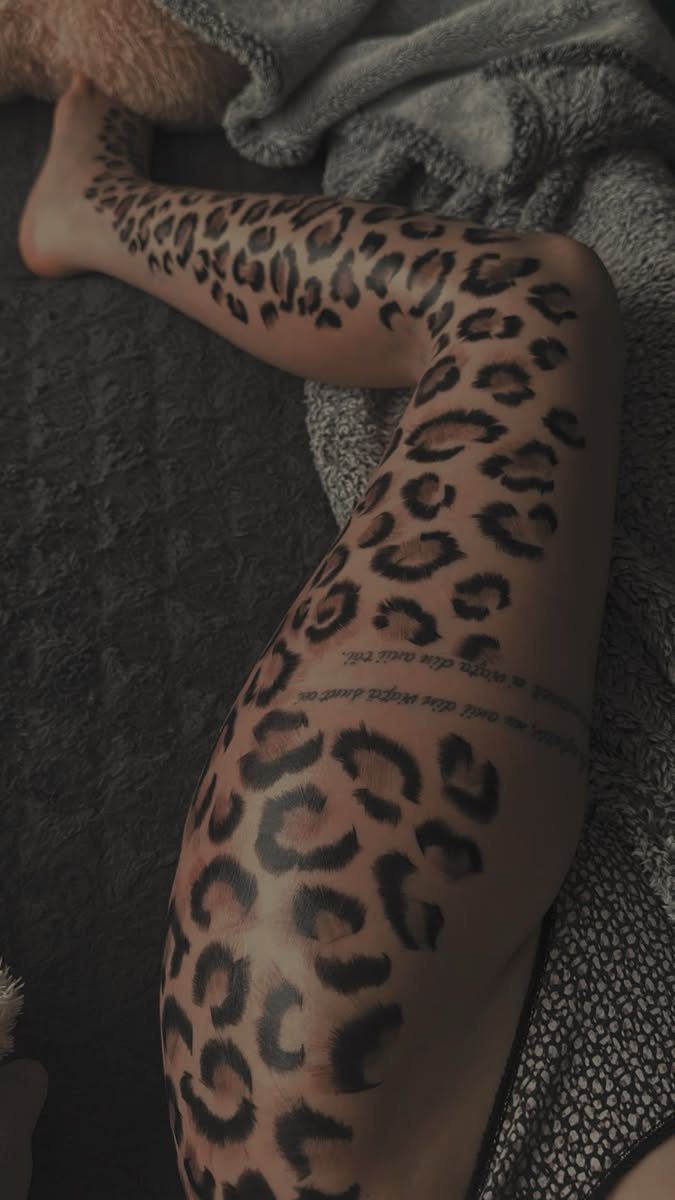 Cheetah Thigh Tattoo: 6 Ideas for Women Who Want Bold Ink 5 A person's leg decorated with a large cheetah print tattoo and cursive script text.