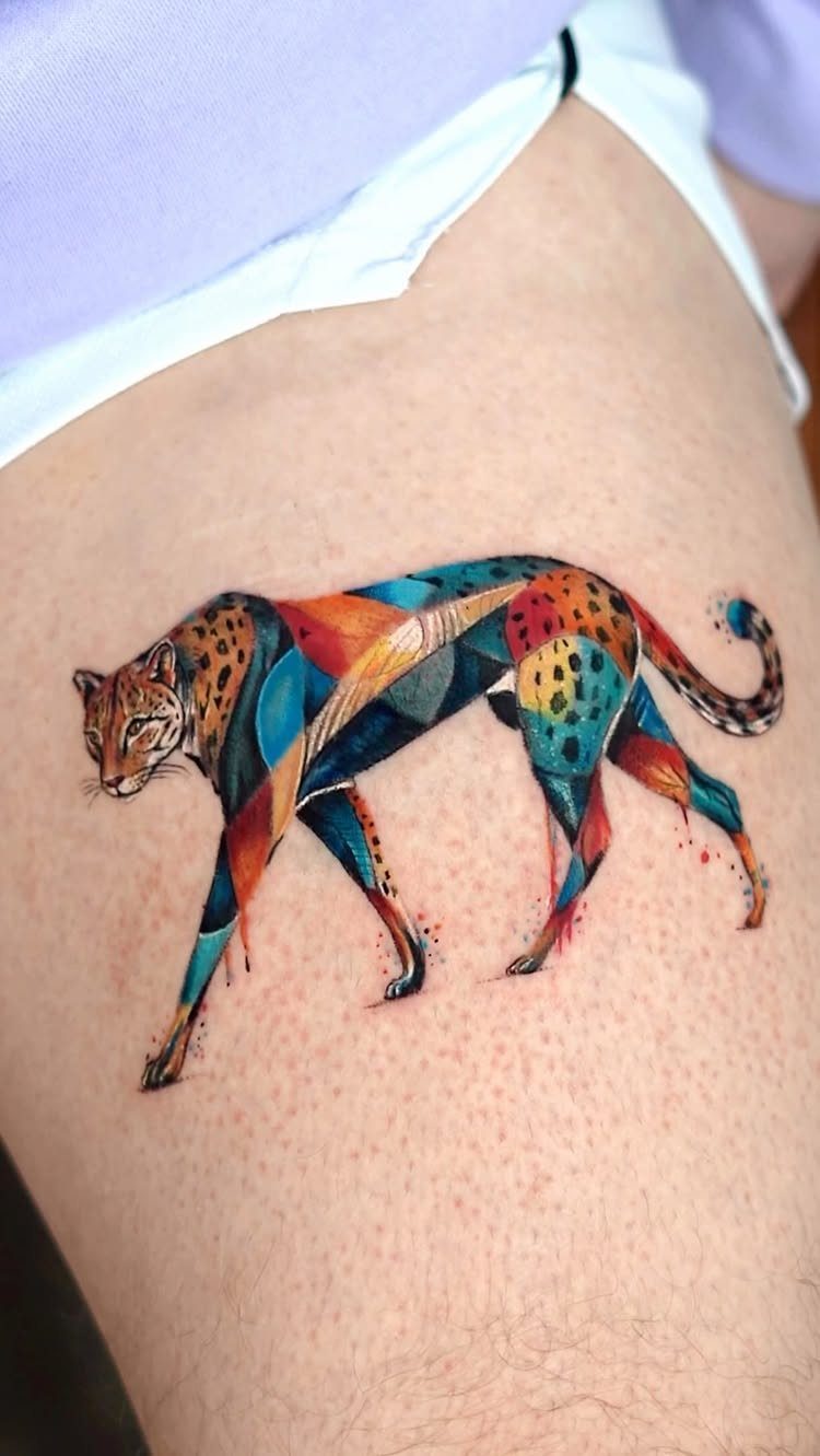 Cheetah Thigh Tattoo: 6 Ideas for Women Who Want Bold Ink 2 A colorful geometric cheetah tattoo walking across a person's thigh skin.