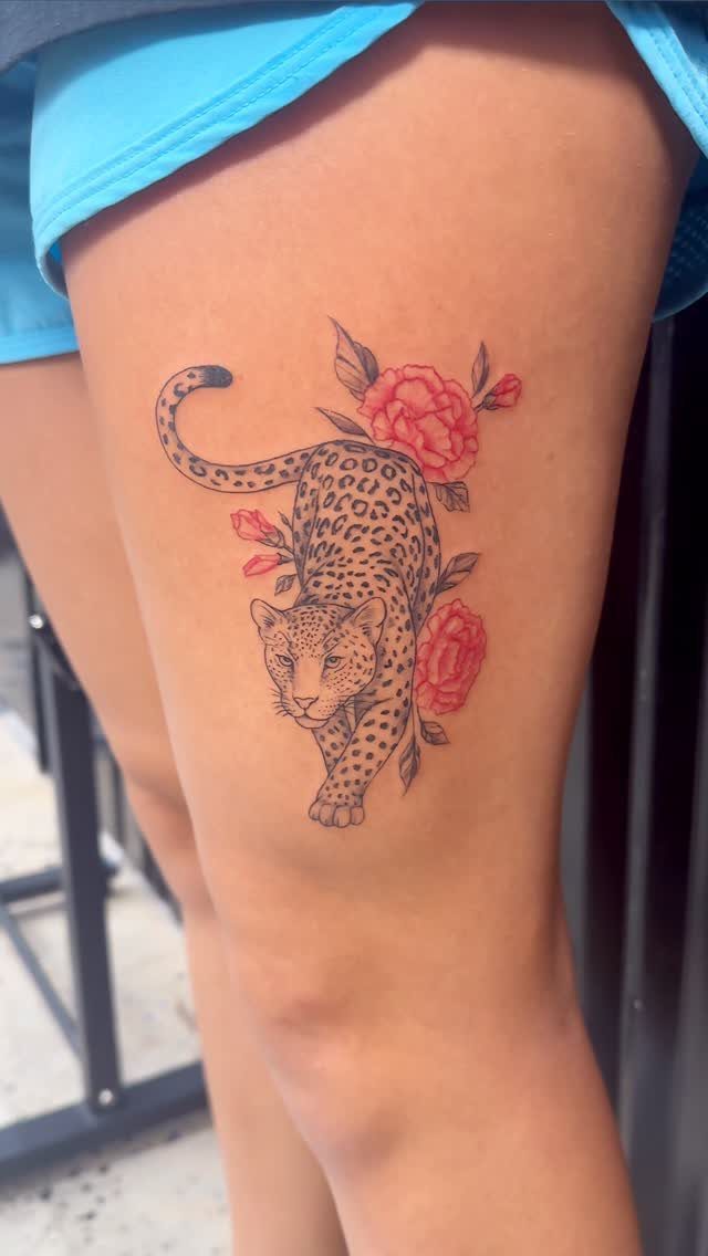 Cheetah Thigh Tattoo: 6 Ideas for Women Who Want Bold Ink 6 A cheetah tattoo with red flowers on a person's thigh.