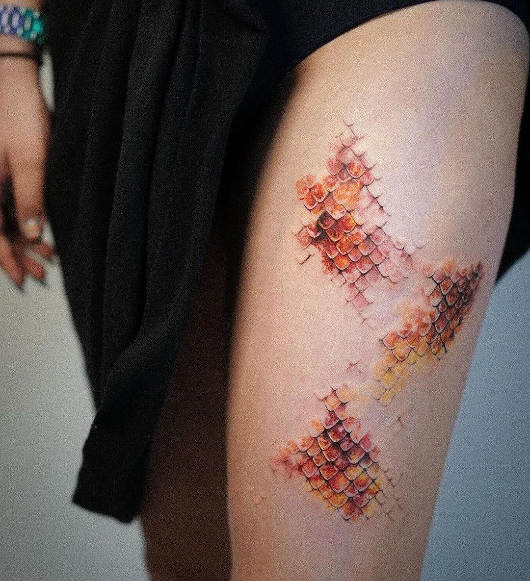Cover Up Tattoo Pattern: 9 Ways to Hide Old Ink or Scars 3 Dragon scale tattoo in orange and red tones on a person's thigh.
