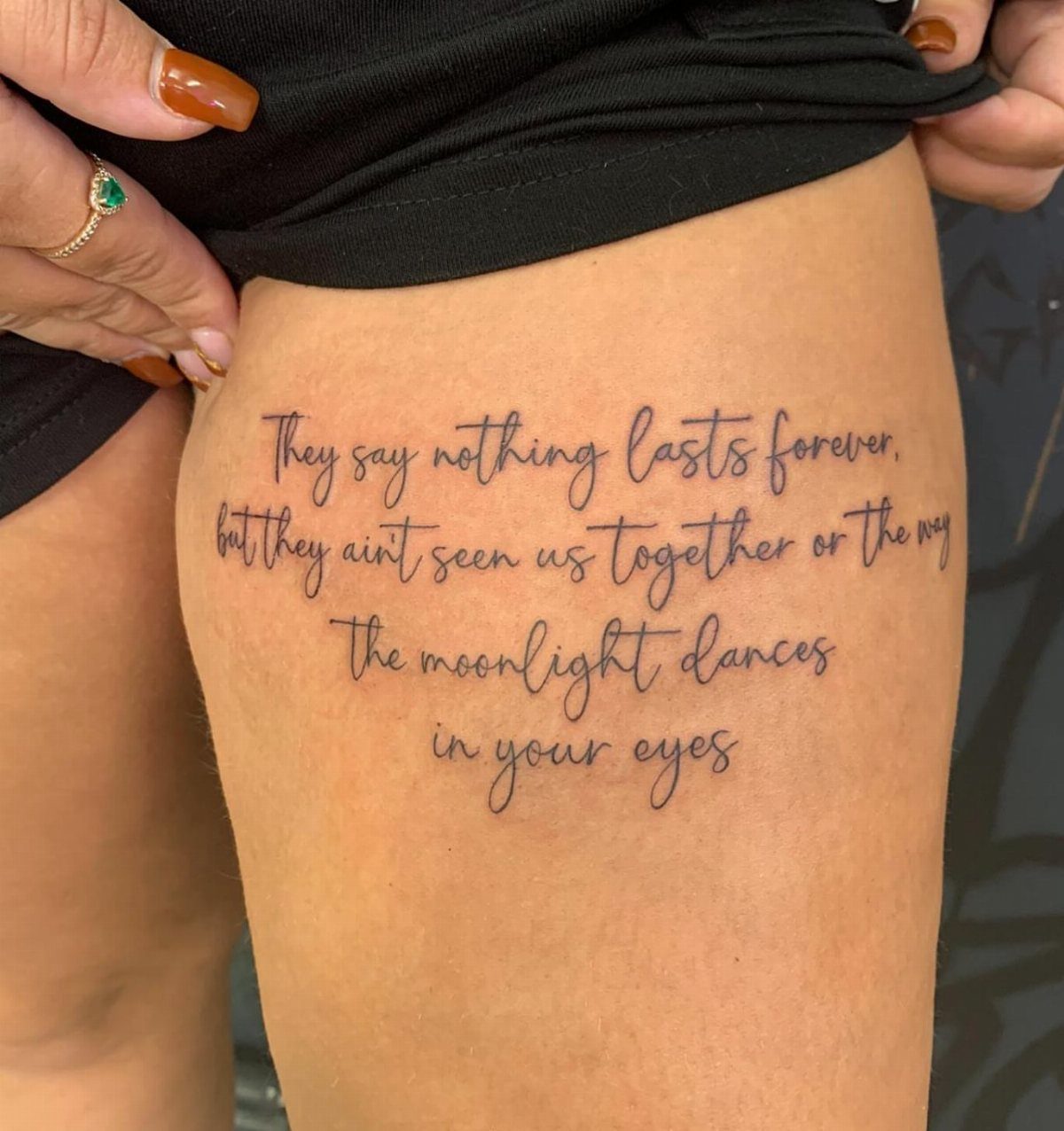 A cursive script tattoo on a person's thigh featuring several lines of poetic text in black ink.