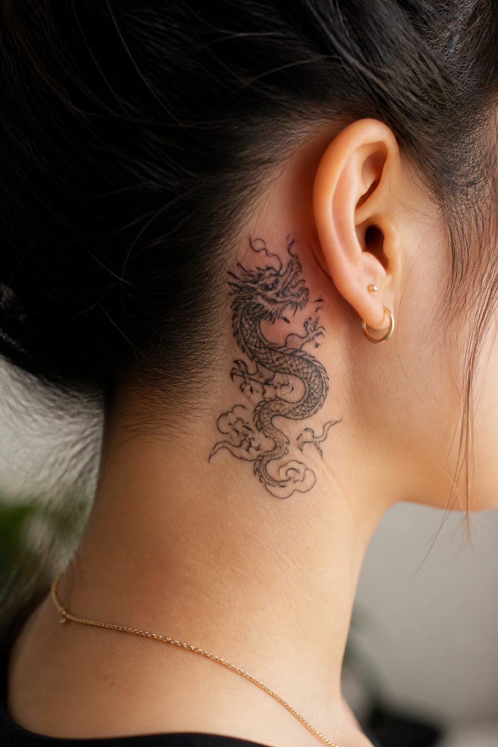 Asian-style dragon tattoo behind the ear with flowing silhouette.