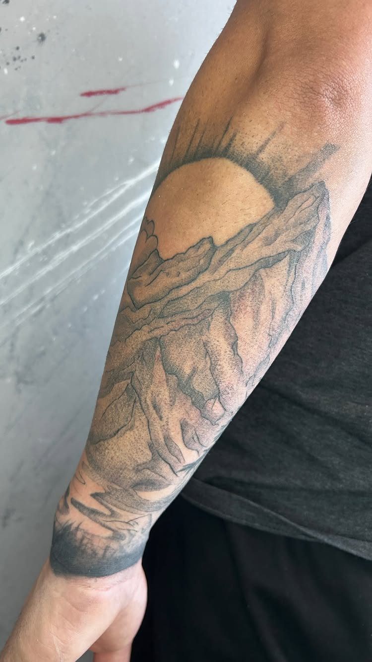 9 Earth Element Tattoo Ideas for Symbols, Scenery and Spirit 7 A black and grey mountain landscape tattoo on a person's forearm with a sun.