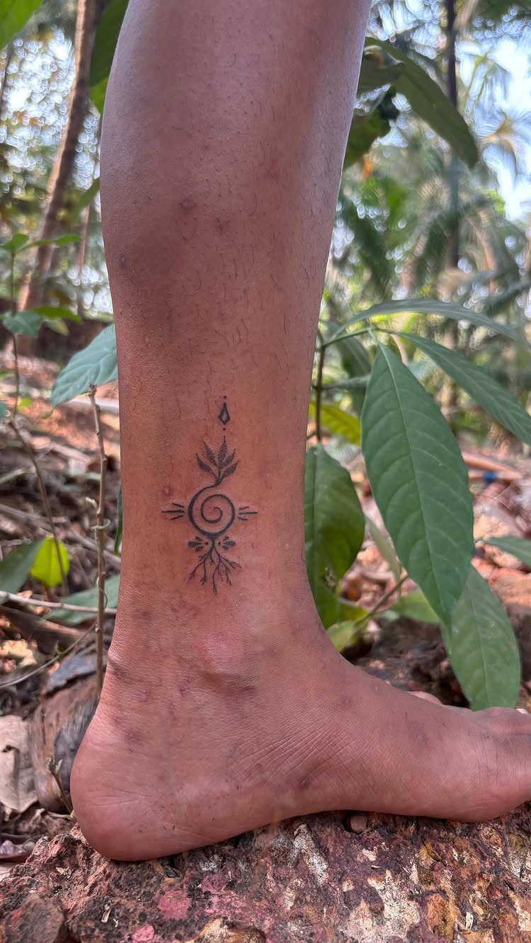 9 Earth Element Tattoo Ideas for Symbols, Scenery and Spirit 1 A minimalist black ink tattoo on a person's ankle featuring a spiral and geometric leaf patterns.