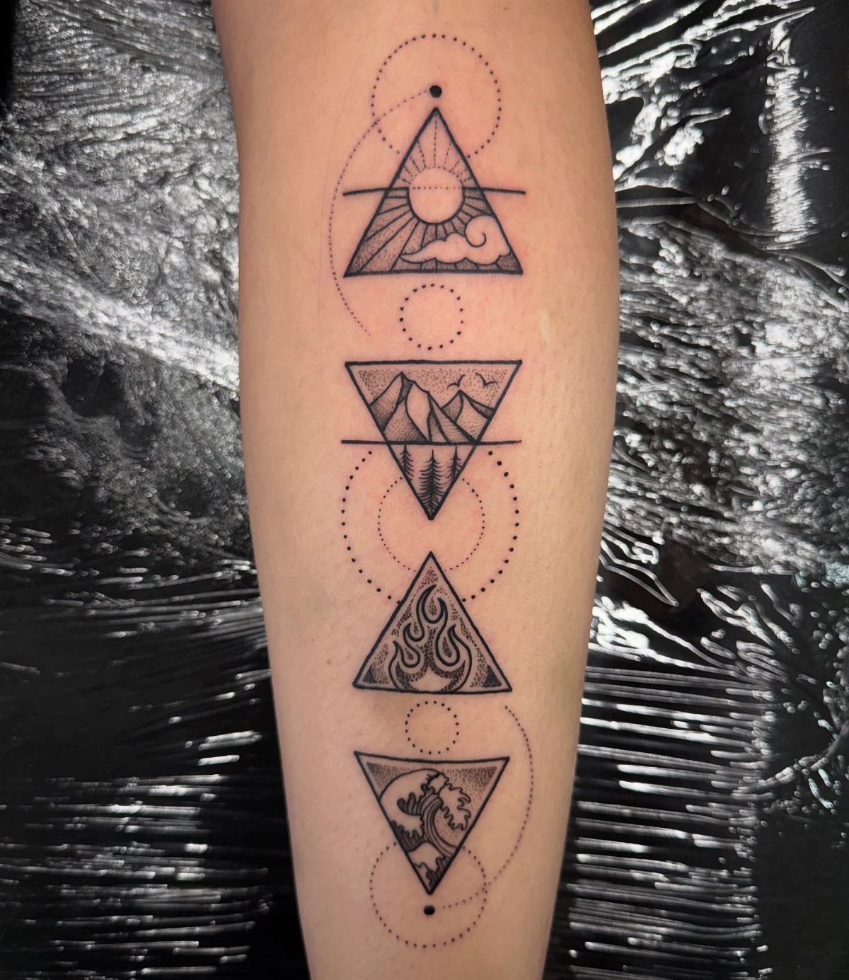 9 Earth Element Tattoo Ideas for Symbols, Scenery and Spirit 5 A forearm tattoo featuring four geometric triangles containing various elemental landscape and nature symbols.