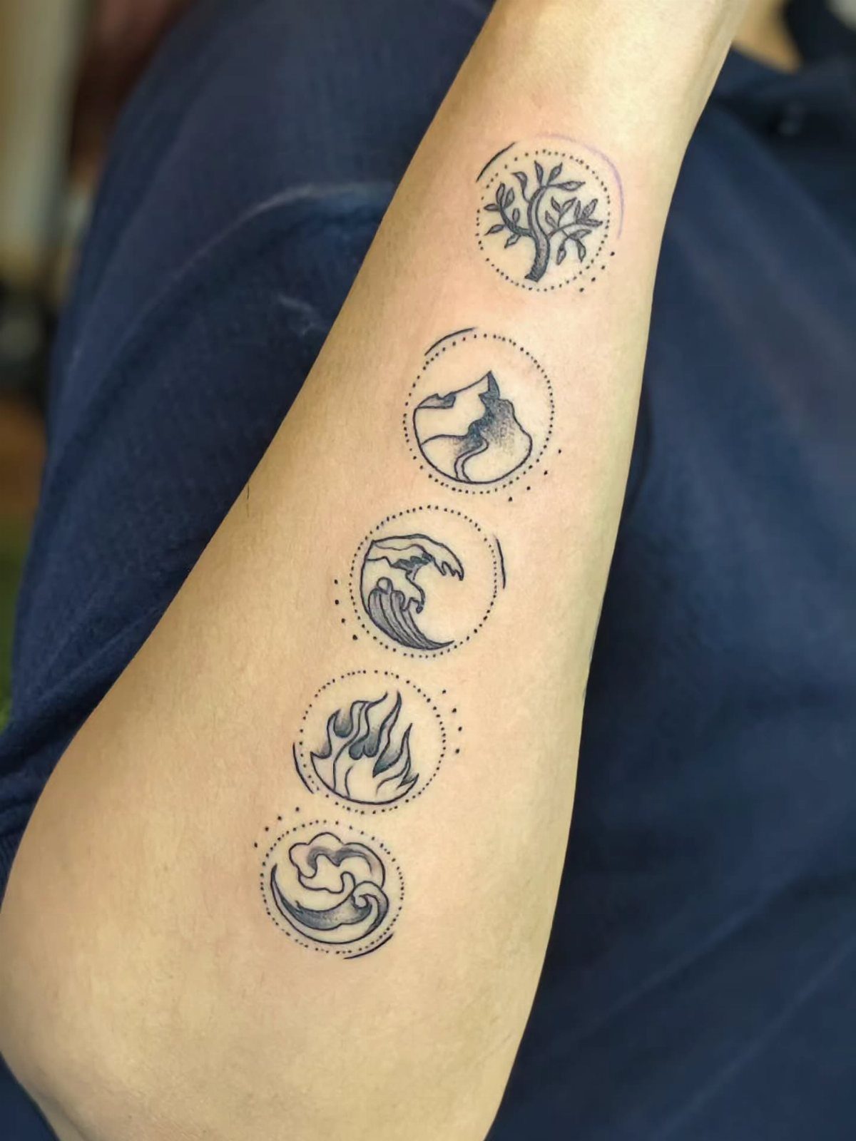 11 Elemental Tattoo Ideas for Your Next Ink 7 Five small circular elemental tattoos arranged vertically on a person's forearm.