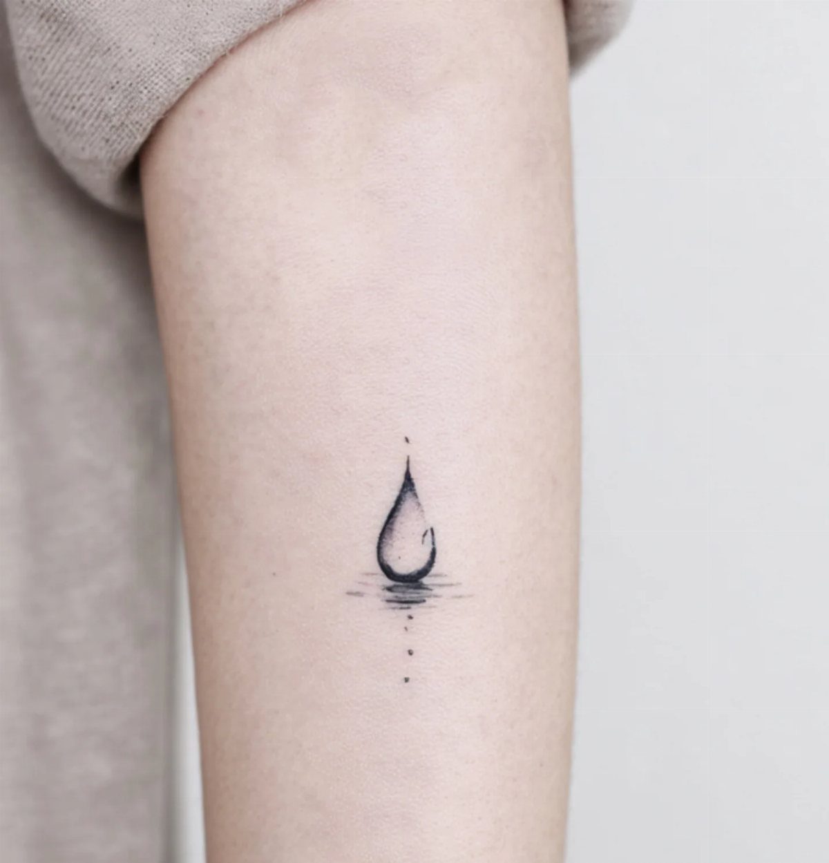 11 Elemental Tattoo Ideas for Your Next Ink 3 A minimalist black ink water droplet tattoo on a person's pale arm.