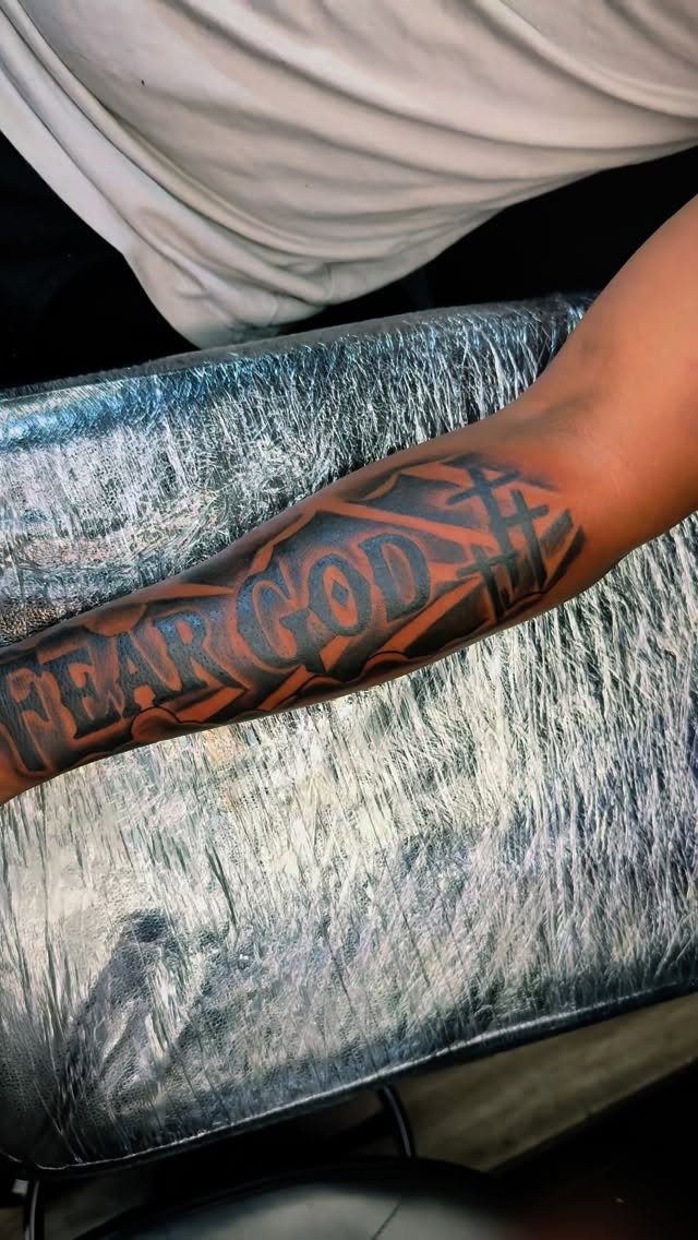 A forearm tattoo with bold black and red lettering reading Fear God.