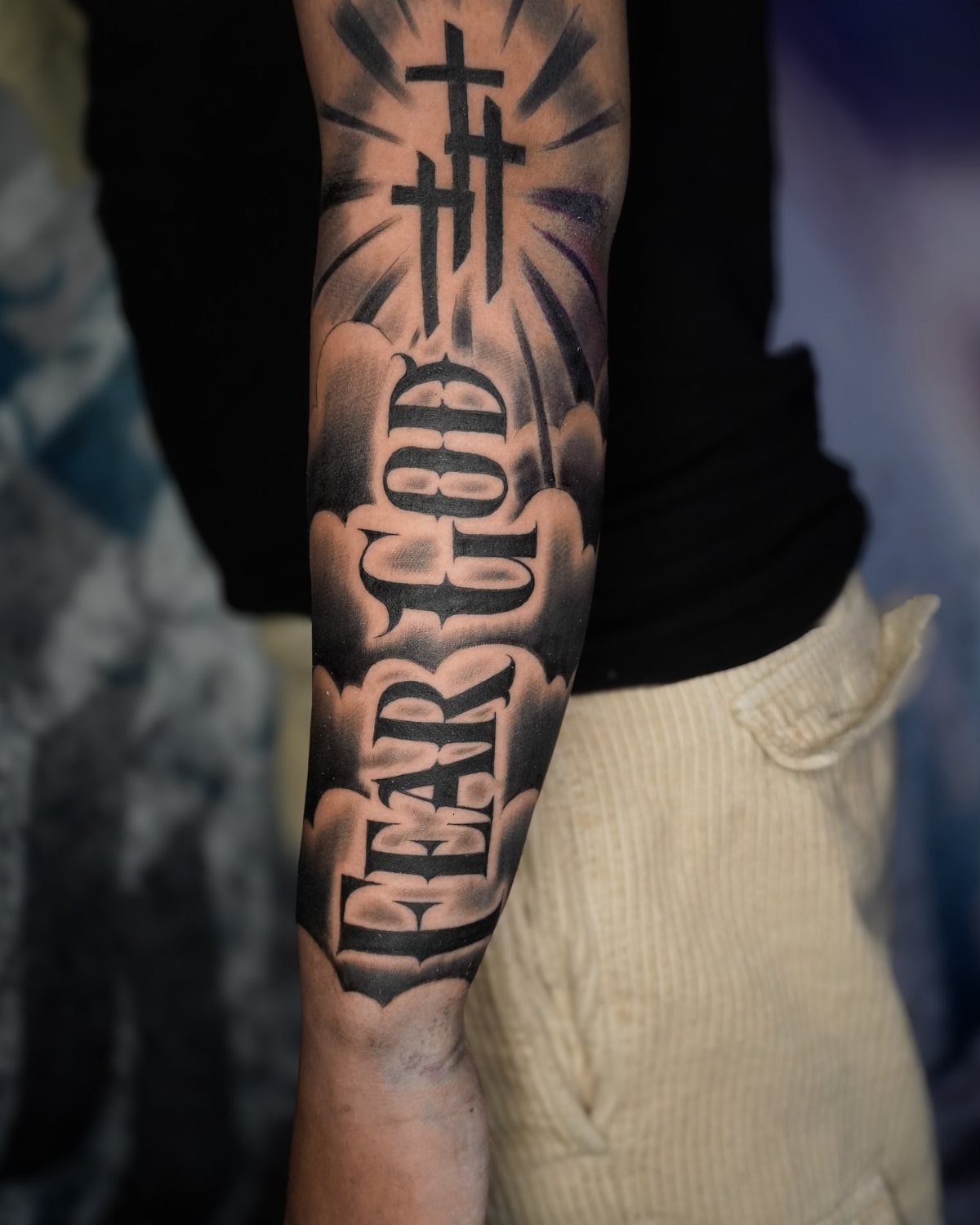 A forearm tattoo with gothic lettering reading FEAR GOD and three crosses above it.