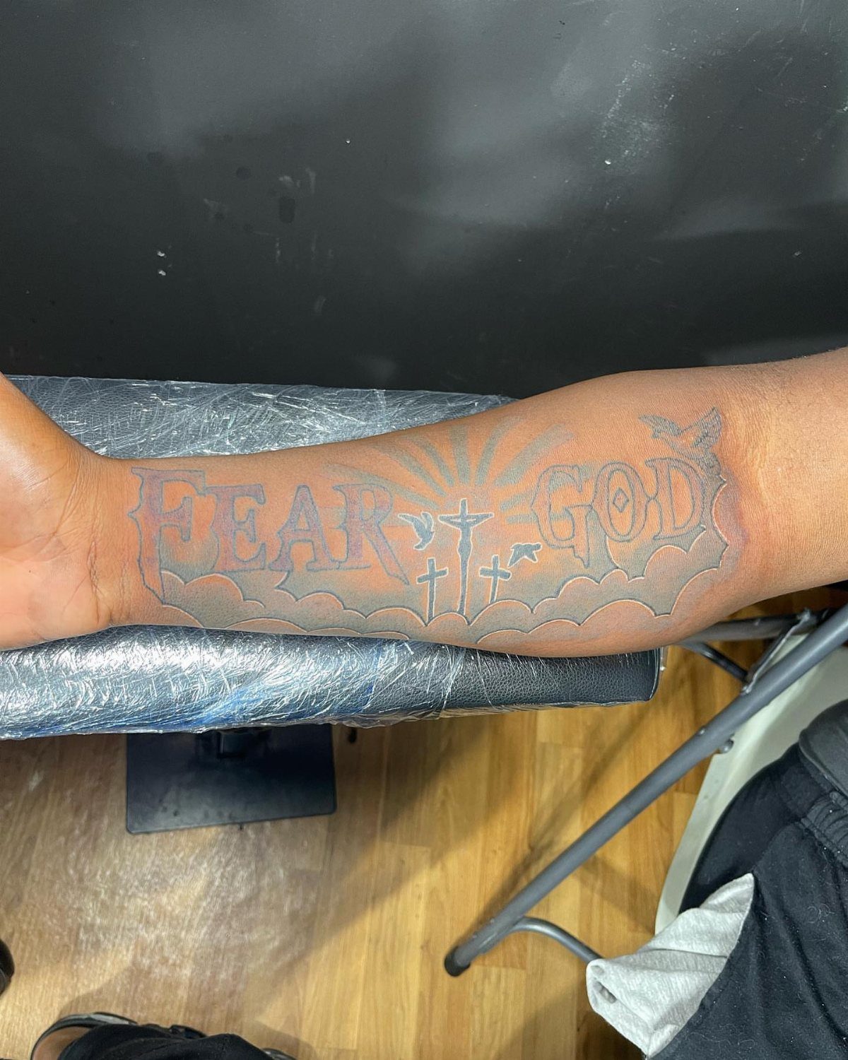 A forearm tattoo with the words FEAR GOD surrounded by clouds and small crosses.