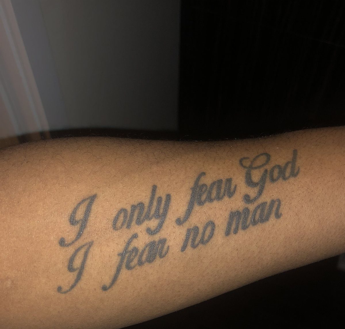 A forearm tattoo in black cursive script reading I only fear God I fear no man.
