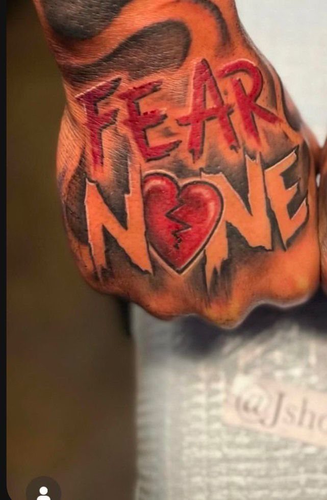 A hand tattoo featuring the words FEAR NONE in red lettering with a broken heart.
