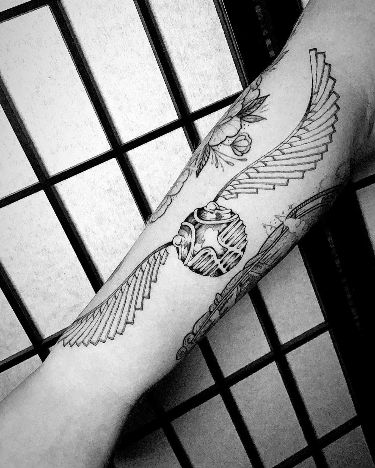 Golden Snitch Tattoo: 7 Styles From Minimalist to Metallic Ink 3 A detailed black and white tattoo of a golden snitch with large wings on a person's forearm.