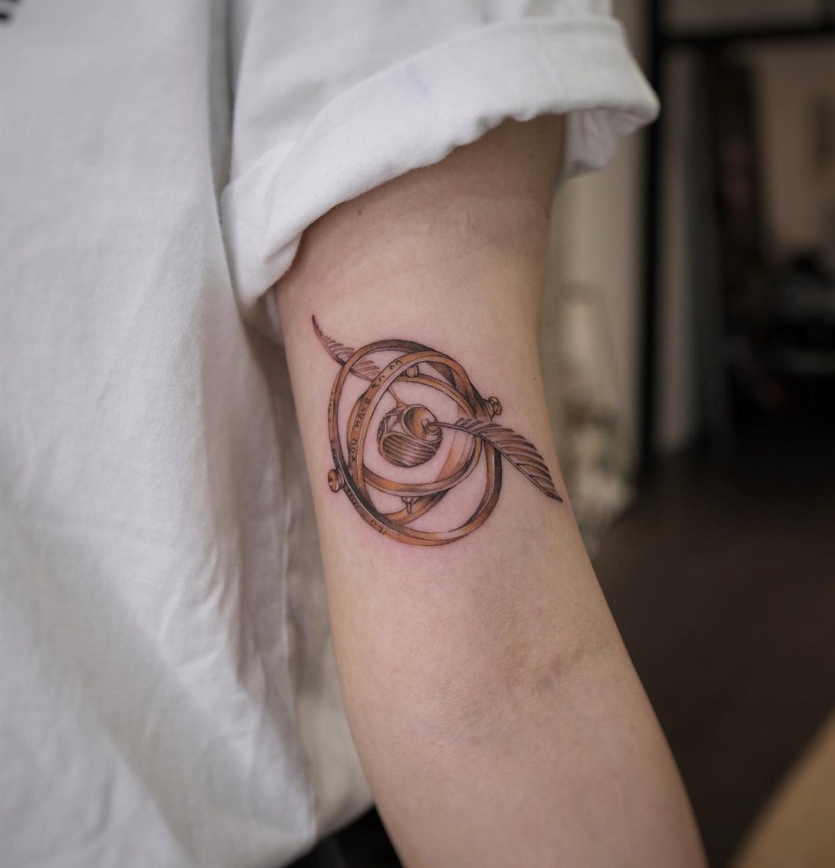 Golden Snitch Tattoo: 7 Styles From Minimalist to Metallic Ink 7 A golden snitch tattoo with circular rings on a person's upper arm.