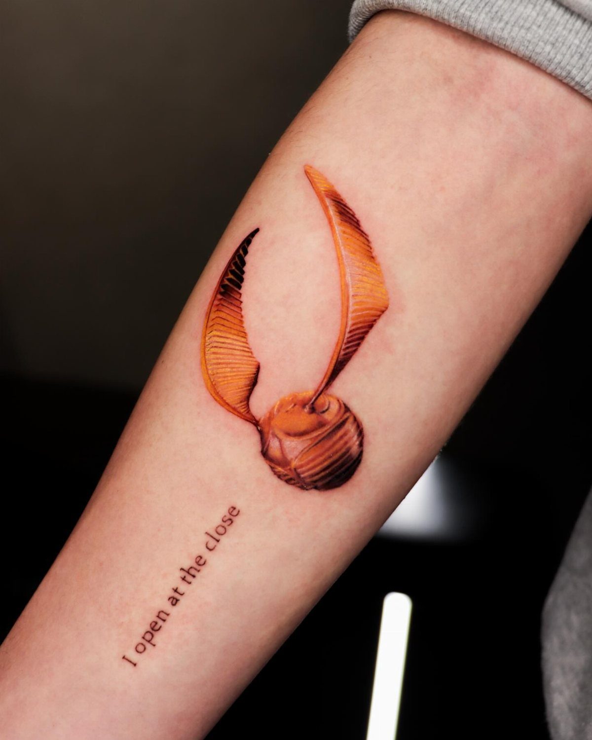 Golden Snitch Tattoo: 7 Styles From Minimalist to Metallic Ink 2 A golden snitch tattoo with text reading I open at the close on an arm.