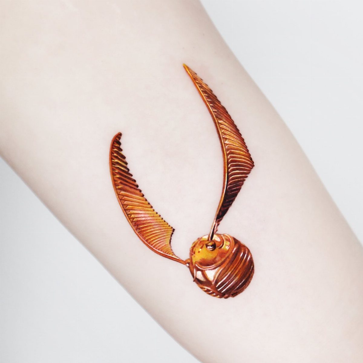 Golden Snitch Tattoo: 7 Styles From Minimalist to Metallic Ink 6 A golden snitch tattoo with metallic bronze wings on a person's arm.