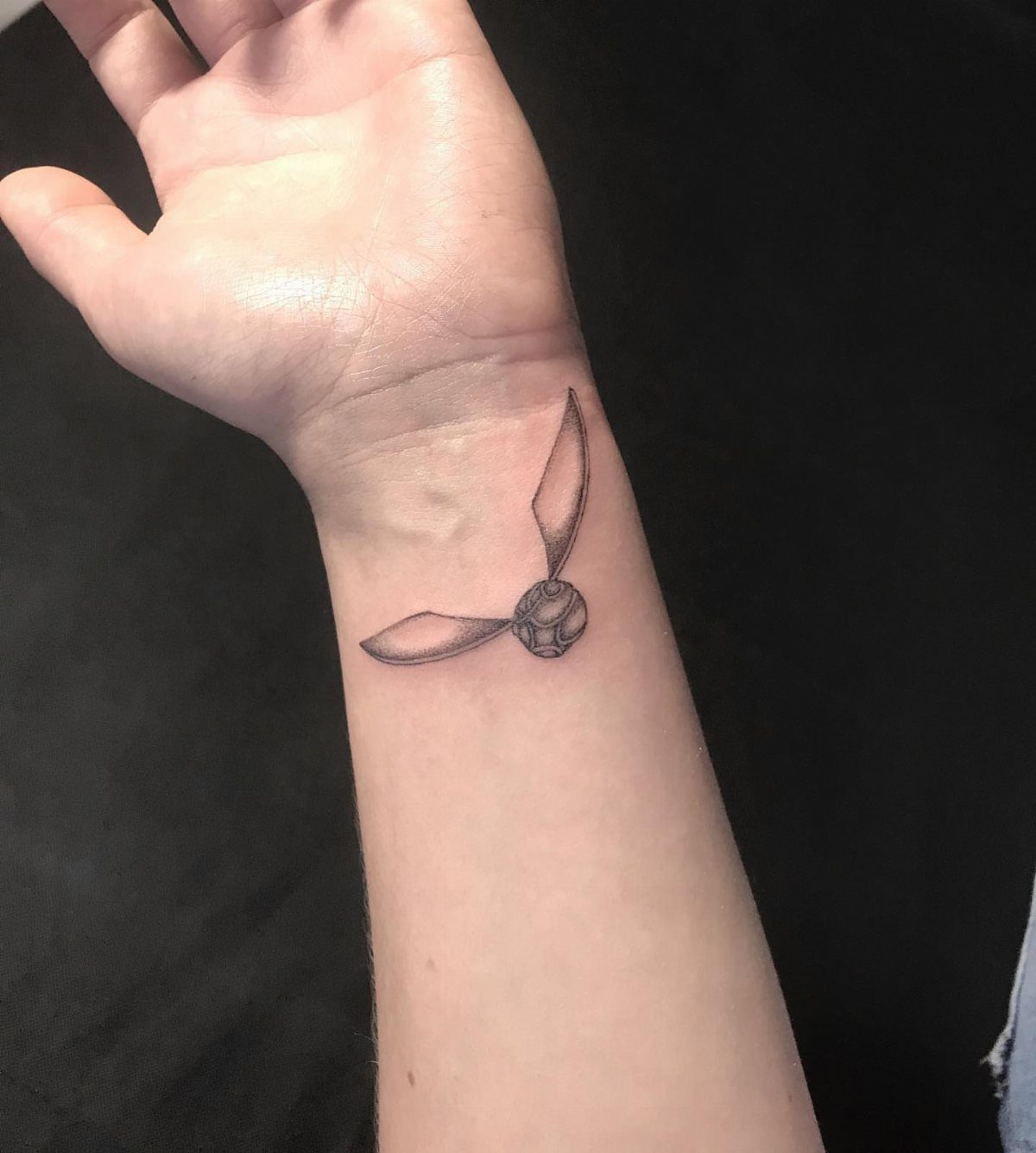 Golden Snitch Tattoo: 7 Styles From Minimalist to Metallic Ink 1 A minimalist black and grey golden snitch tattoo on a person's inner wrist.
