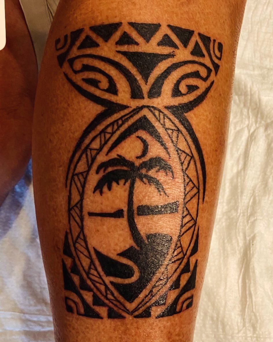 A large black tribal tattoo on a person's leg featuring a palm tree and geometric patterns.