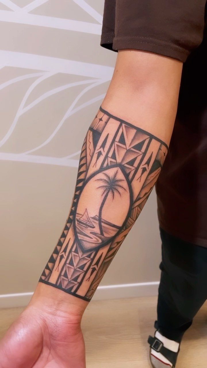 A forearm tattoo featuring a palm tree and ocean waves surrounded by geometric tribal patterns.