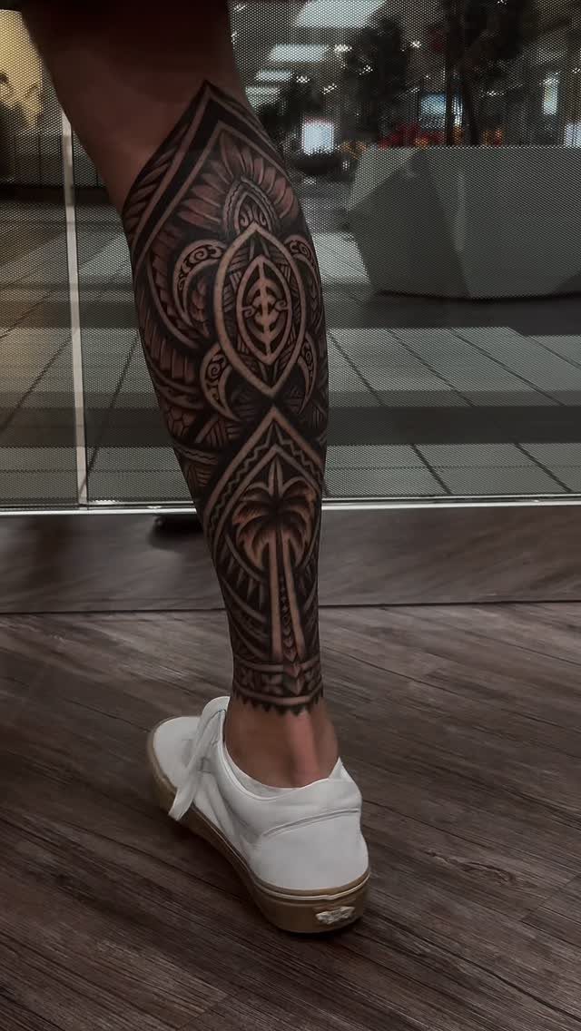 A large black ink tribal tattoo with geometric patterns covering a person's lower leg.