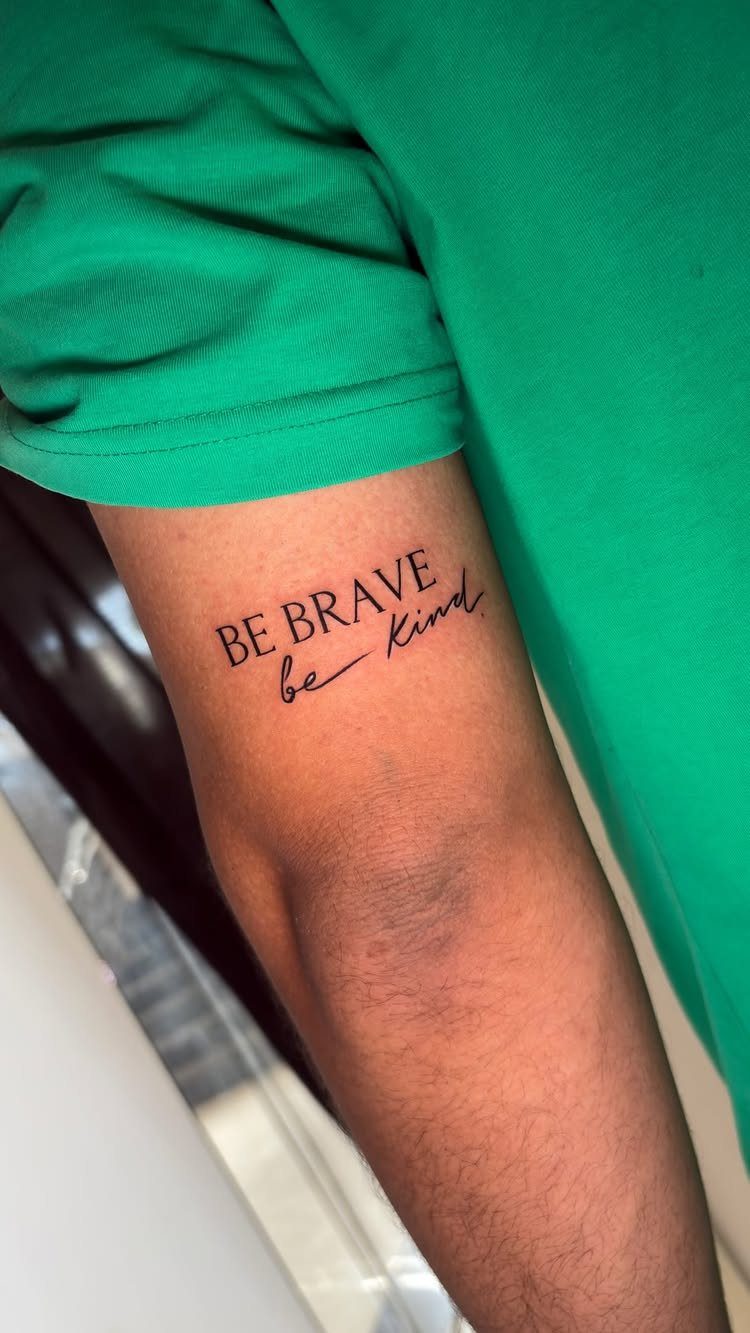 Have Courage and Be Kind Tattoo: 6 Designs Worth Committing To 1 A black ink tattoo on a person's arm reading BE BRAVE be kind.