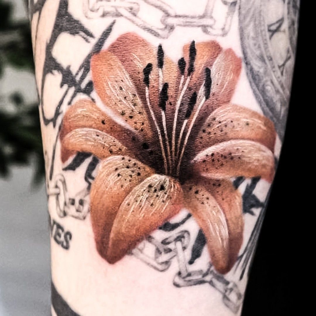 Jungkook Tattoo: 3 Design Ideas From Hands to Full Sleeve 2 A detailed orange lily tattoo with dark stamen on a person's arm.