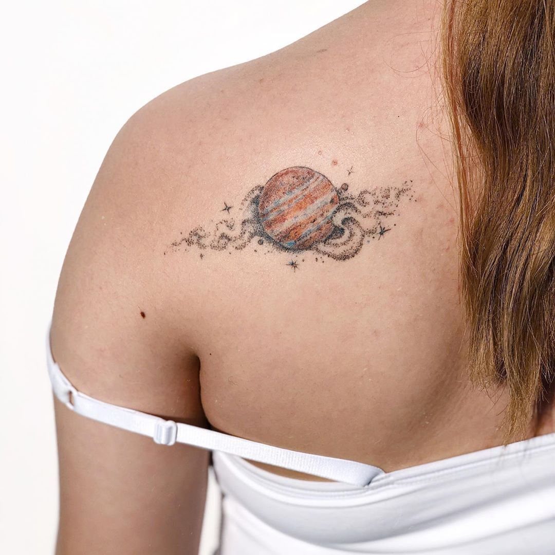 5 Jupiter Tattoo Ideas for Celestial Ink That Stands Out 4 A small Jupiter planet tattoo with dotwork stippling on a person's shoulder.