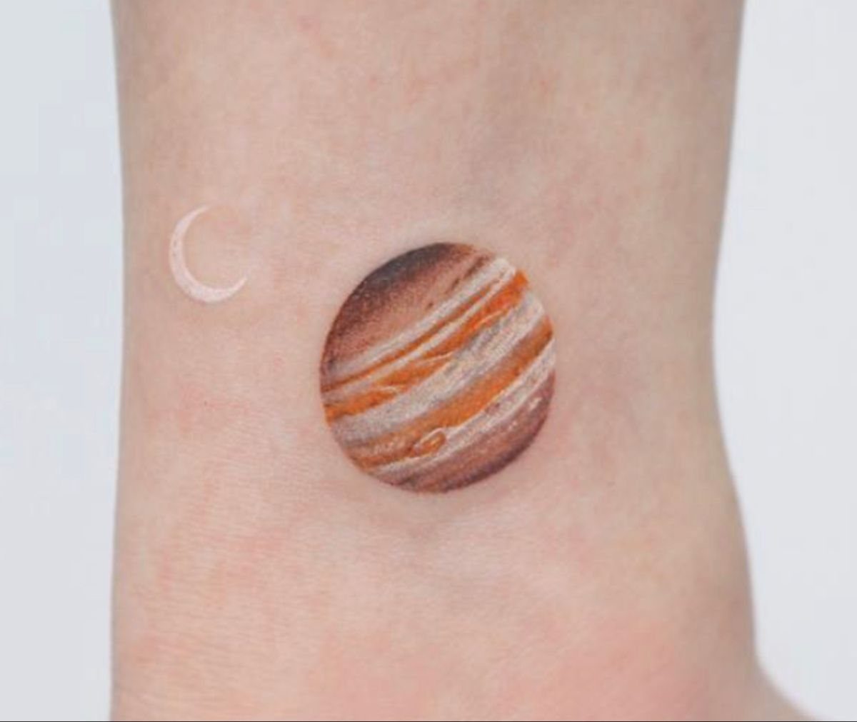 5 Jupiter Tattoo Ideas for Celestial Ink That Stands Out 5 A realistic Jupiter and crescent moon tattoo on a person's wrist.