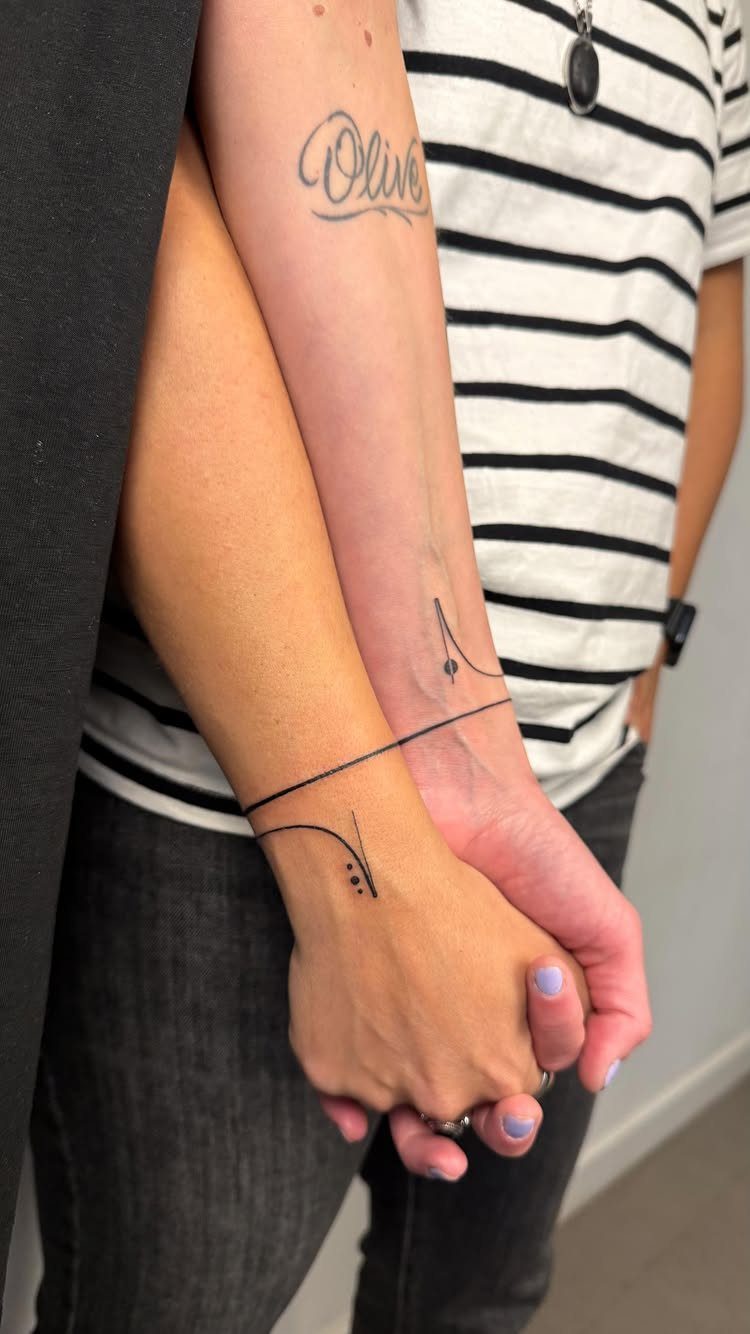 9 Minimalist Couple Tattoo Ideas Unique and Subtle for Lasting Ink 3 Two people holding hands, displaying matching minimalist line tattoos on their wrists and a script tattoo.